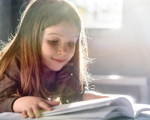 Girl with long hair leaning over a book and reading with a slight smile on her face