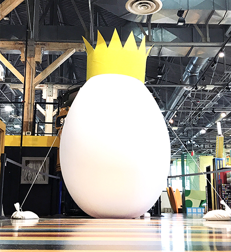 Giant egg wearing a paper crown in front of a train